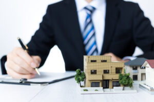 住宅の模型のそばで書類に記入する手元